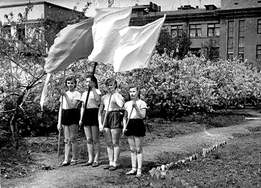 Три ученицы с флагами на фоне школьного сада.